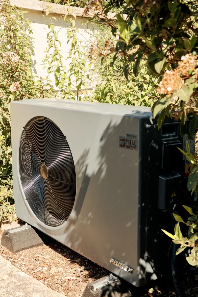 Pompe à chaleur Poolex Silverline installée en extérieur avec végétation, vue avant en léger contre-jour