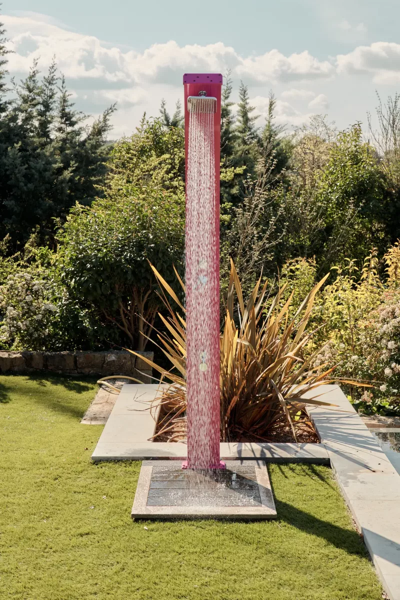 Douche solaire Spring 30L rose – vue de profil près d’une piscine (installation extérieure)